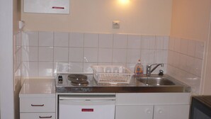 Una cocina compacta con armarios blancos, lavavajillas integrado, un lavabo y un microondas.