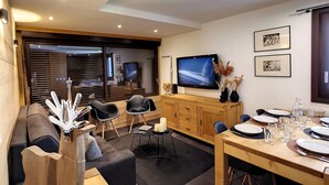 Een moderne woonkamer met een flatscreen-televisie, houten kasten en een eethoek voor vier personen.