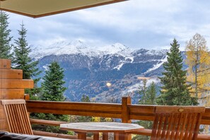 A wooden deck with a table and chairs, overlooking a mountainous landscape with snow-capped peaks and a forested valley. - Charming flat located in the quiet region of Chemin des Vernes, in 5 minutes of the ski lift of Médr (Verbier)