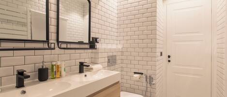A modern bathroom with white subway tiles, a white sink, a toilet, and a shower.