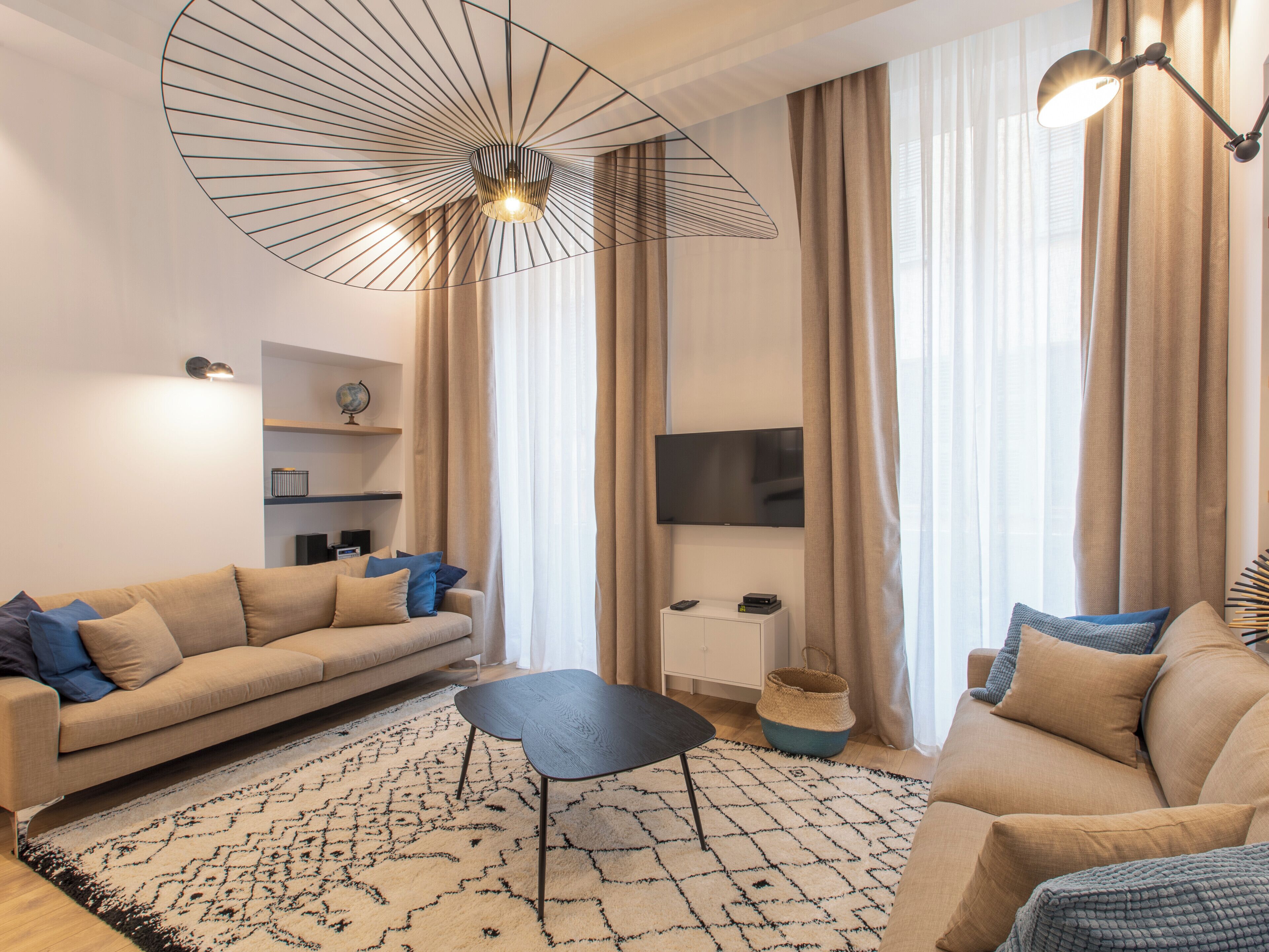 A modern living room with a sofa, a coffee table, a TV, and a unique ceiling light fixture.