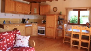 Eine gemütliche Küche mit Holzausbau, einem Esstisch mit Stühlen, einer Couch mit gemusterten Kissen und einer Uhr an der Wand.