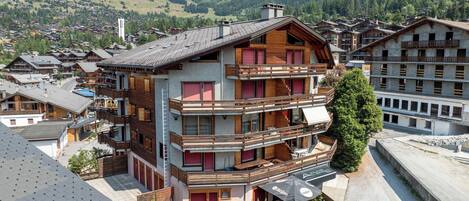 Un edificio de varios pisos con balcones, rodeado por un paisaje montañoso.