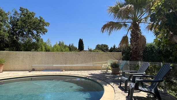 A swimming pool with a curved edge, surrounded by a concrete deck. There are lounge chairs and a small table near the pool. - Maisonnette with private pool in the Alpilles (Maussane-Les-Alpilles)