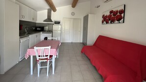 A compact kitchen with white cabinets, a microwave, a sink, and a dining table with a checkered tablecloth. A red sofa is against the wall, and a clock is on the wall. - Maisonnette with private pool in the Alpilles (Maussane-Les-Alpilles)