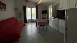 A compact living space with a kitchenette, a dining area with a table and chairs, a red sofa, and a sliding glass door leading to an outdoor area. - Maisonnette with private pool in the Alpilles (Maussane-Les-Alpilles)