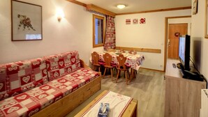 Una habitación acogedora con sofá, una mesa de comedor con sillas, televisión y un mueble de madera.
