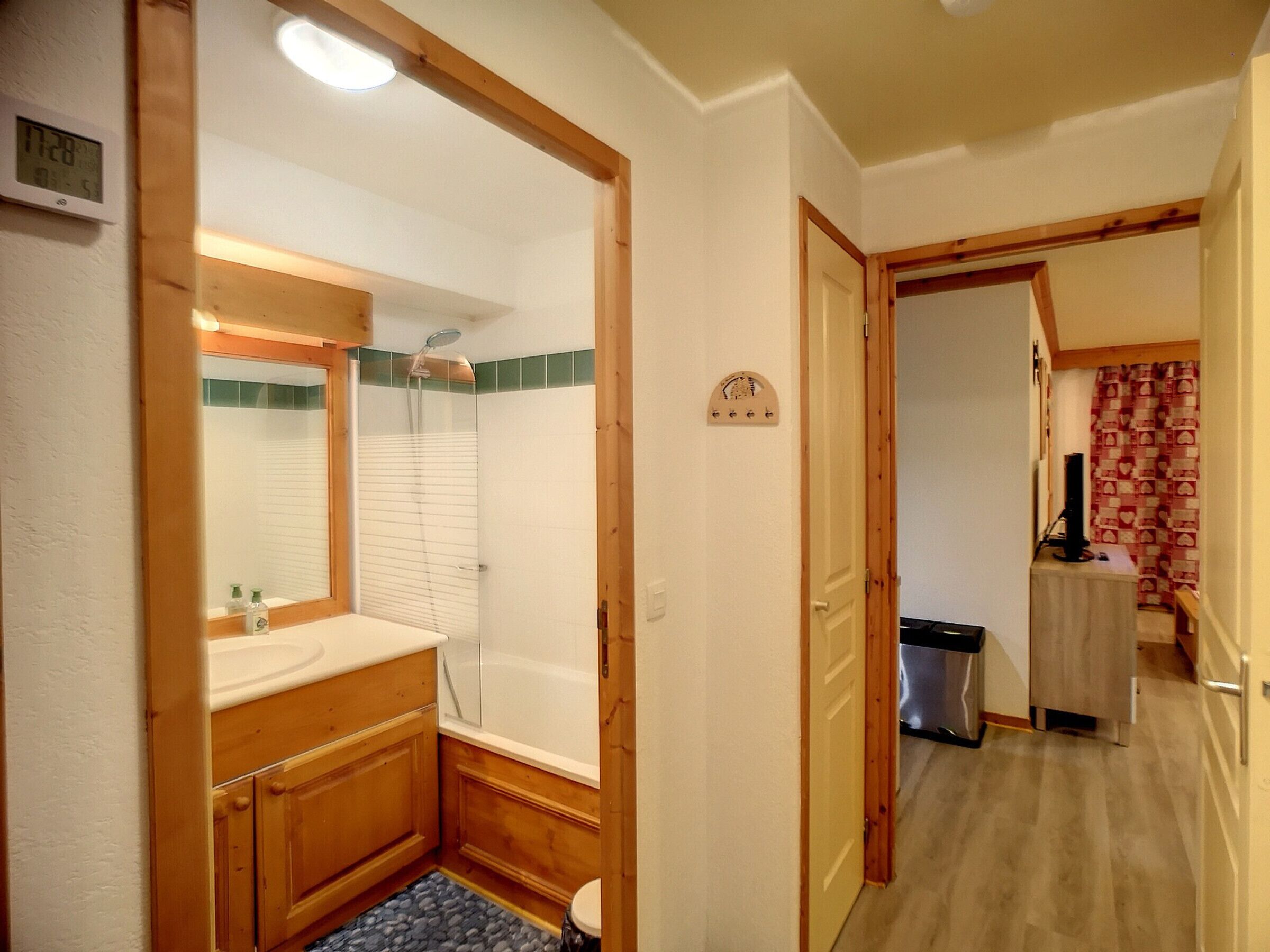 A bathroom with a wooden vanity, a mirror, a shower enclosure, and a small trash bin.