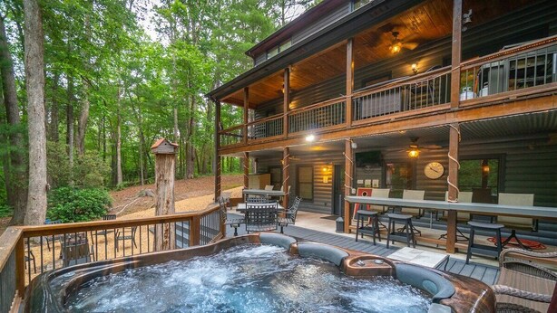 Ein Whirlpool mit Holzterrasse, Sitzgelegenheiten im Freien und ein rustikales Blockhaus mit Balkon.