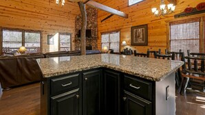 Ein Holzblockhaus-Interieur mit Kamin aus Stein, Granit-Arbeitsplatten und einem Essbereich.