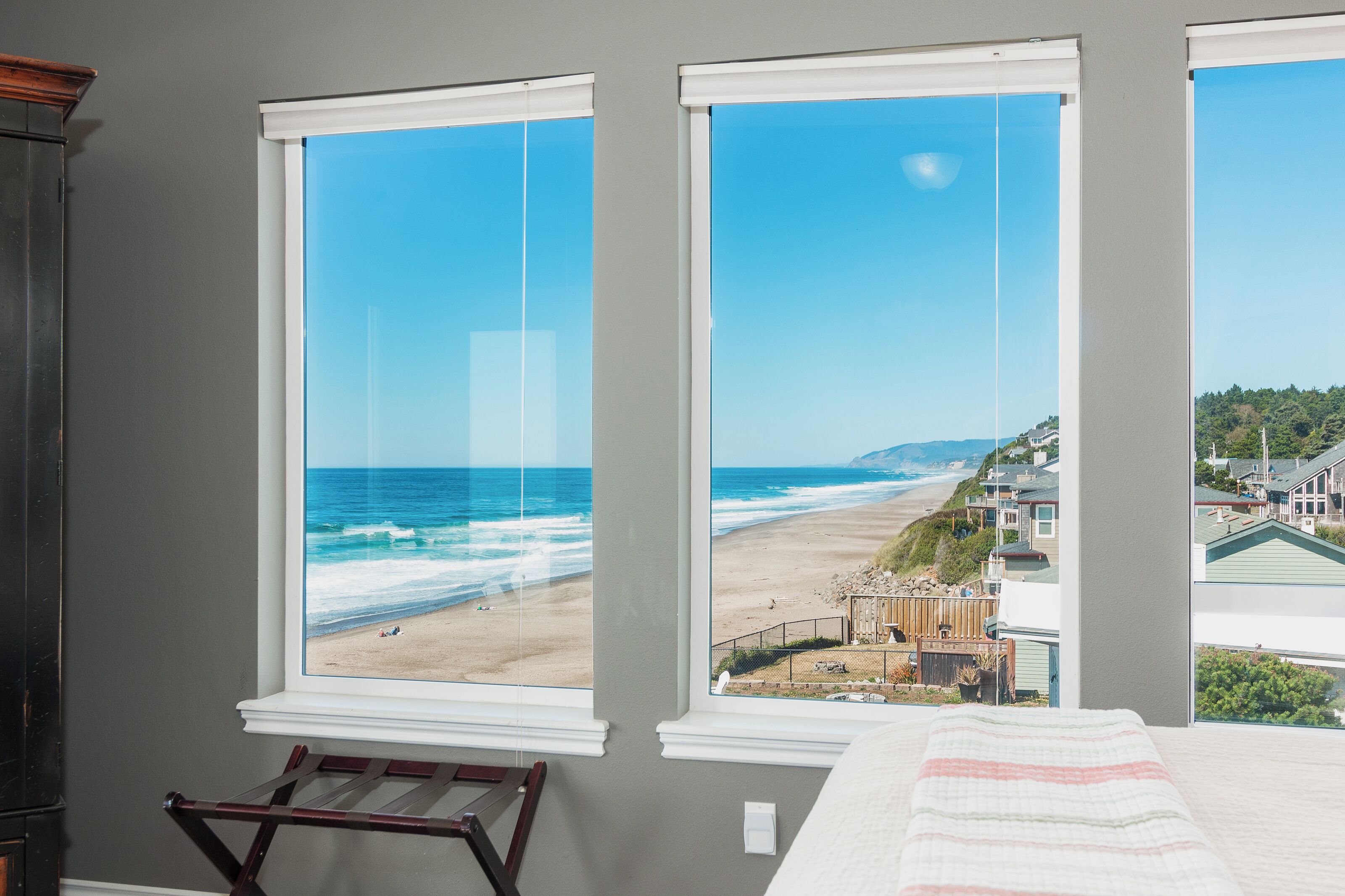 A bedroom with a large window overlooking a beach and a residential area.