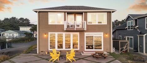 A two-story house with a balcony, a patio with outdoor seating, and a stone wall in the foreground.