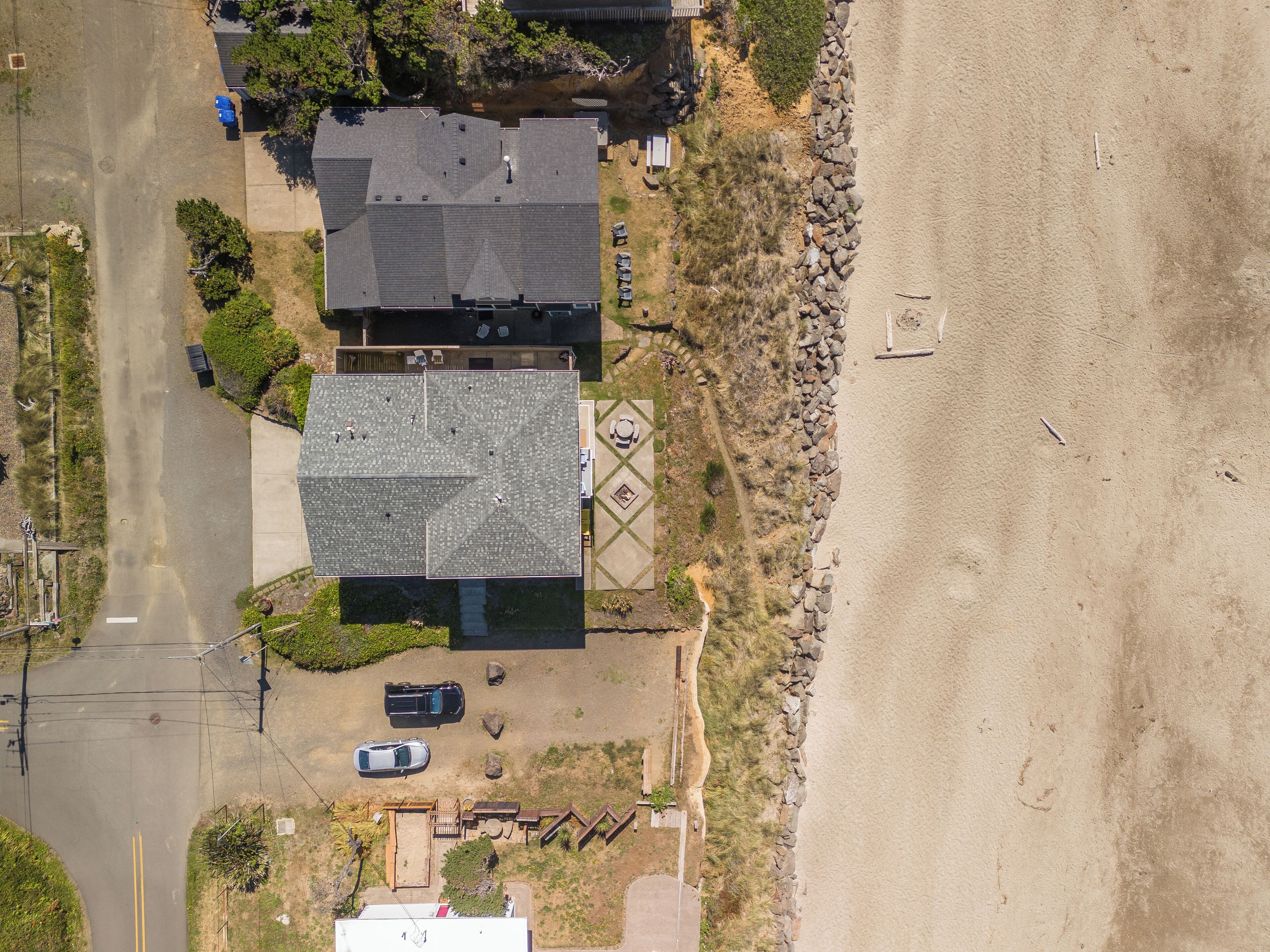 An aerial view of a property with a large house, a driveway, a parking area, and a beach.