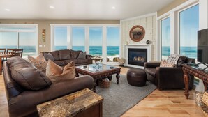 A spacious living room with a large window overlooking the ocean, a fireplace, and a cozy seating area. - Ocean Front Luxury Home (Gleneden Beach)