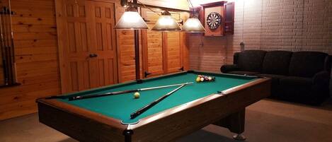 Una mesa de billar con bolas, un dardo y un sofá en una habitación con paredes y puertas de madera.