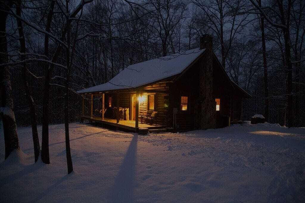 A log cabin with a porch, surrounded by snow-covered ground and trees.