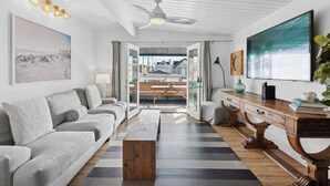 A modern living room with a sofa, coffee table, and a view of the city through a glass door. - 37th Street beach house, steps to sand - Air conditioning, bikes and parking! (Newport Beach)