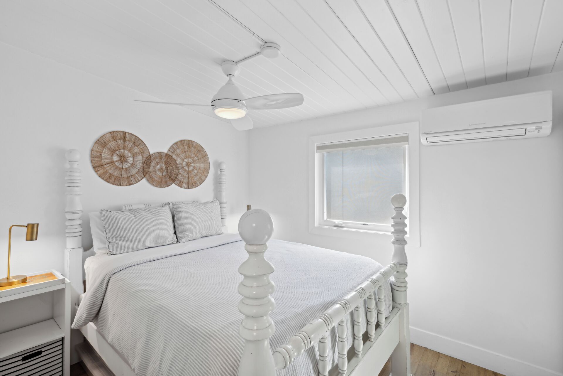 A bedroom with a white bed, a ceiling fan, a window, and wall decor.