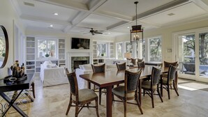 A spacious dining area with a large wooden table and wicker chairs, a fireplace, and a ceiling fan. - Sunset Rentals | Capri 2 (Hilton Head Island)