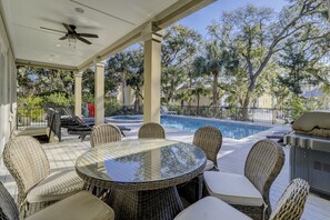 Un patio al aire libre con mobiliario de mimbre, una piscina y un ventilador de techo.