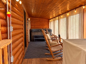 A log cabin interior with a cozy seating area, a hot tub, and a view through large windows.