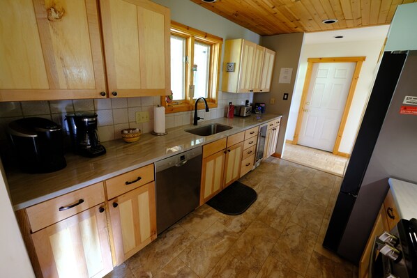 Una cocina con armarios de madera, lavavajillas, pileta y refrigerador.