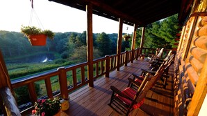 Eine Holzterrasse mit Sitzgelegenheiten und hängenden Pflanzgefäßen mit Blick auf bewaldetes Gebiet.