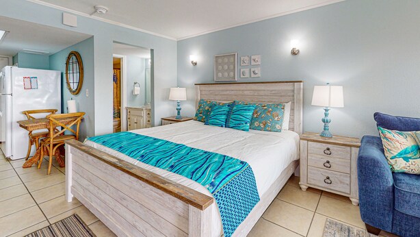 Une chambre à coucher comprenant un lit, des tables de chevet, une chaise, un bureau et un réfrigérateur.