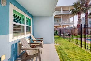 Ein Gebäude mit blauer Fassade, einer überdachten Veranda mit Adirondack-Stühlen und einem eingezäunten Garten mit Schwimmbad.