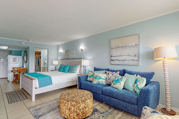 Ein Schlafzimmer mit einem Bett, einem blauen Sofa, einem runden Hocker und einer Lampe.