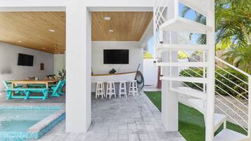 Un espace extérieur moderne doté d’une piscine, d’une terrasse en bois, d’un bar et d’un escalier blanc.