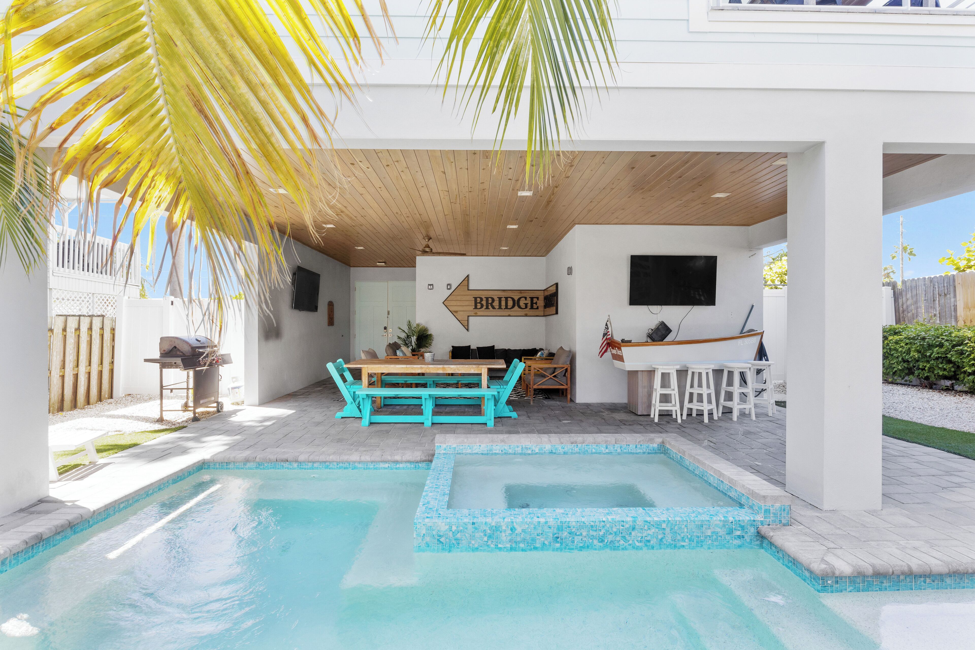 Un espace piscine avec une terrasse en bois, une table et des chaises, et un panneau indiquant l’emplacement d’un pont.