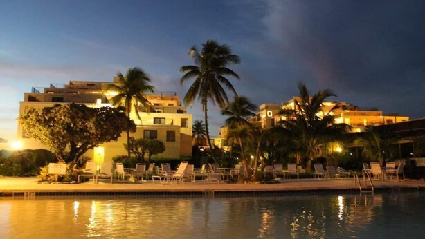 A resort with a swimming pool, palm trees, and beachfront buildings at dusk. - Beach Front Studio For Rent in Freeport Grand Bahamas , Port Lucaya (Freeport)