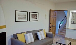 Ein Wohnzimmer mit einer Couch, zwei gerahmten Bildern, einer Holztür und einer Treppe.