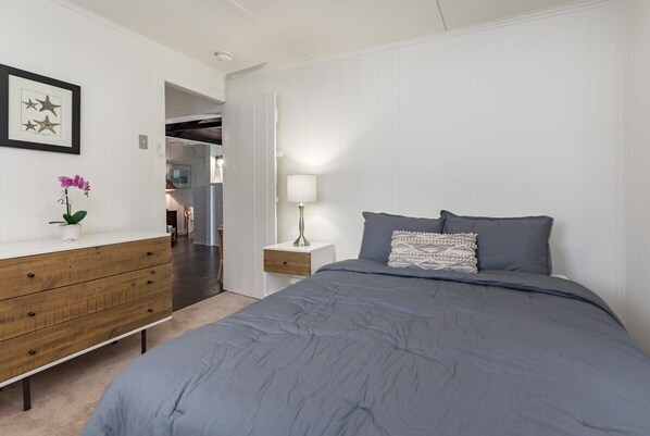 A bedroom with a bed, a dresser, a nightstand, a lamp, and a door leading to another room.