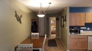 A compact kitchen with a microwave, a small sink, and wooden cabinets. A dining area with a wooden table and chairs is visible, and a hallway leads to a bedroom. - Closest building to the main lift. (Frisco)