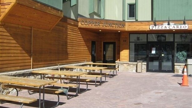 An outdoor seating area with wooden tables and benches, a building with signs for 'Copper Junction' and 'Pizza Carlo'. - Closest building to the main lift. (Frisco)
