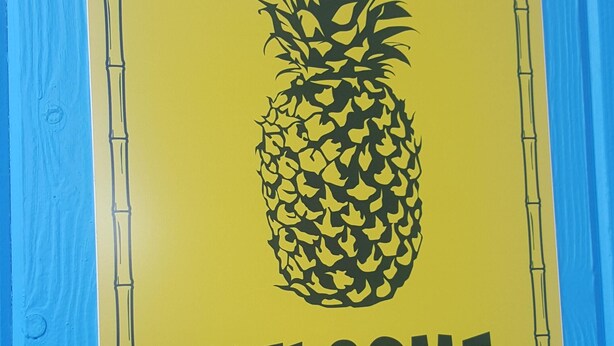 Une enseigne d’accueil ornée d’un motif d’ananas sur un fond en bois bleu.