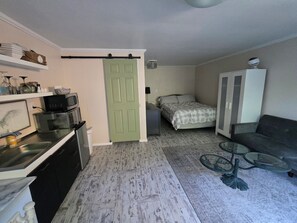 Un espacio habitable compacto con kitchenette, una cama, un sofá y una mesa de vidrio.