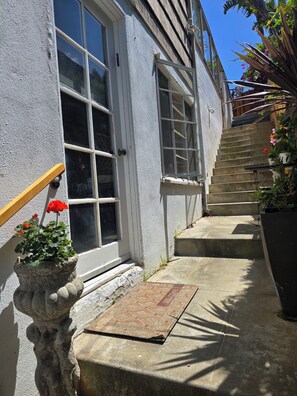 Ein Haus mit Haustür, einer Treppe, die zu einer Veranda führt, und einem Topf mit roten Blumen.
