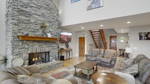 A spacious living room with a stone fireplace, comfortable seating, a staircase, and artwork on the walls. - Large Luxury Home with Great Views (Banner Elk)
