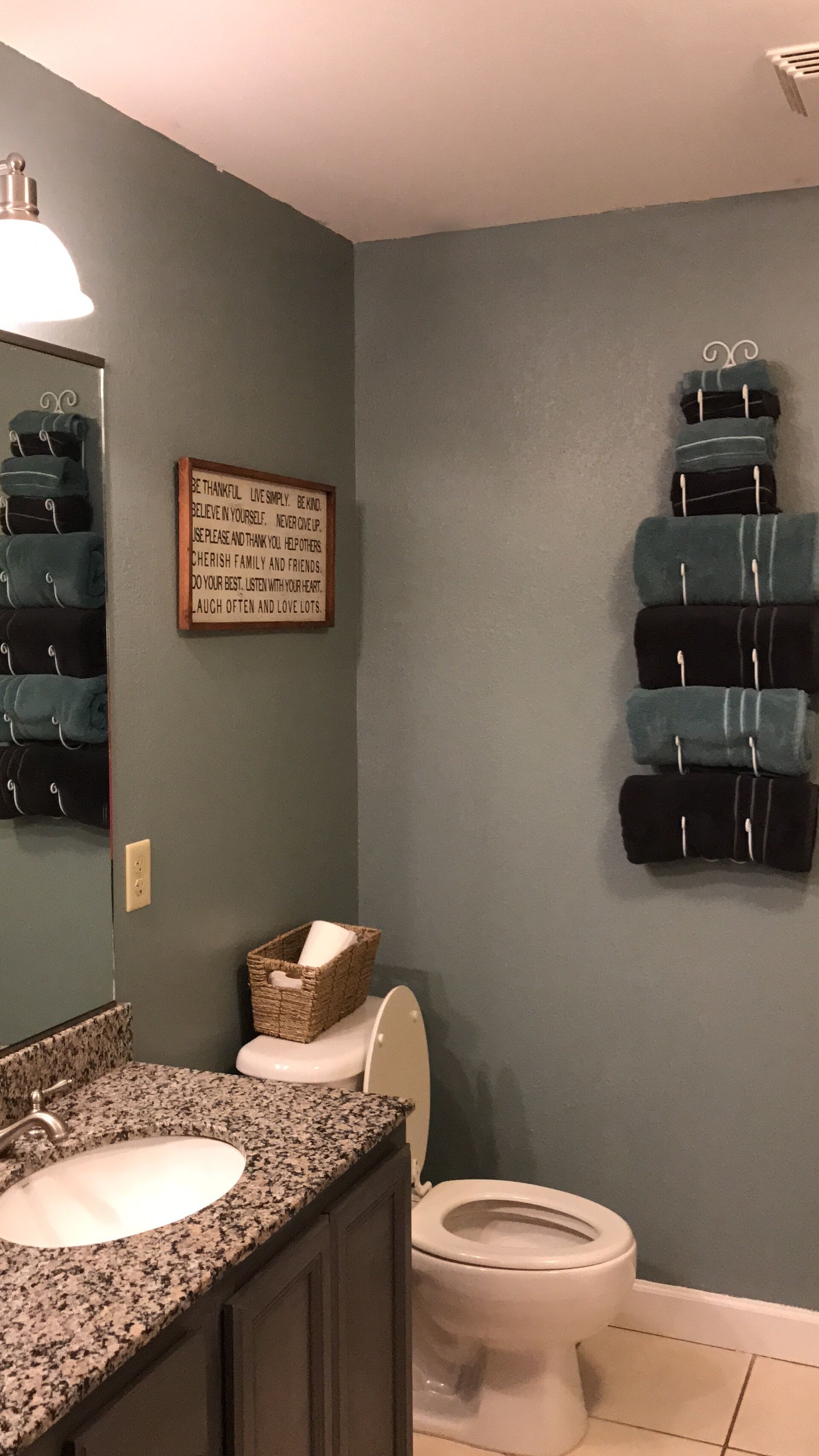 A bathroom with a granite countertop sink, a white toilet, and a wall-mounted towel rack with folded towels.