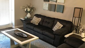 Ein Wohnzimmer mit einem dunkelgrauen Sofa, einem weißen Couchtisch und einem gemusterten Teppich.