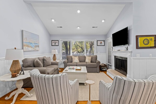 A living room with a fireplace, a television, and a window with blinds. - Fairway Dunes 27 - Screen Porch Golf Course View! (Isle of Palms)