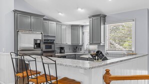 A modern kitchen with grey cabinets, stainless steel appliances, a marble island, and a window with blinds. - Fairway Dunes 27 - Screen Porch Golf Course View! (Isle of Palms)