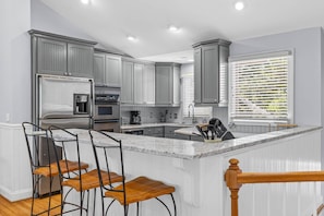 A modern kitchen with grey cabinets, stainless steel appliances, a marble island, and a window with blinds. - Fairway Dunes 27 - Screen Porch Golf Course View! (Isle of Palms)