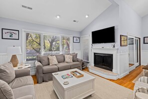 A living room with a fireplace, a television, and a large window with blinds.