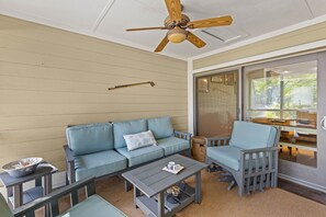 A covered patio area with a blue sofa, a dining table, and a ceiling fan. - Fairway Dunes 27 - Screen Porch Golf Course View! (Isle of Palms)