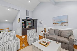 A living room with a sofa, two striped armchairs, a coffee table with books, a lamp, and a painting on the wall.