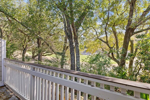 A wooden deck with a white railing overlooking a grassy area with trees.